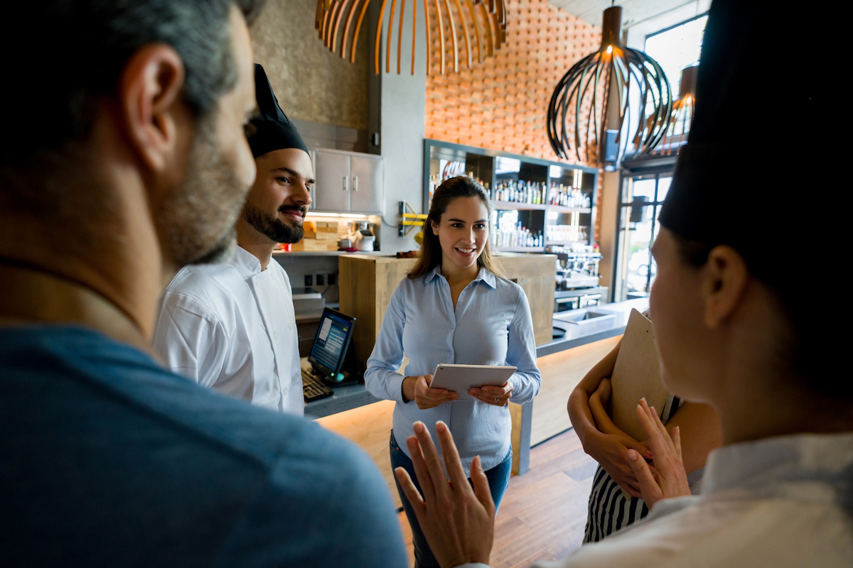 Happy staff talking to their boss in a meeting at a restaurant and smiling